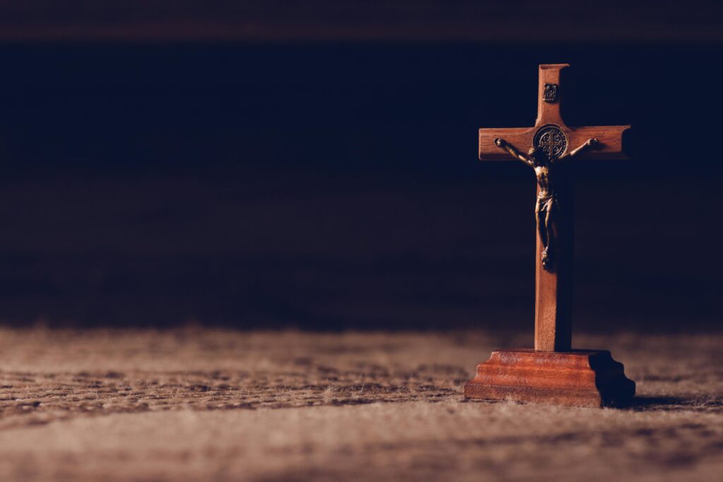 A solitary wooden crucifix stands on a carpet, casting a shadow in dim ambient lighting symbolizing peace and reflection.